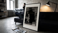 Man walking with torch in dark hall print in a slim black frame leaning on a dark sofa in a concrete print studio