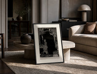 Man walking with torch in dark hall print in a black frame leaning on a travertine table in a sunlit lounge