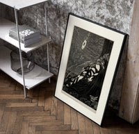 Bound man swarmed by rats poster in a black frame leaning beside a shelf in a raw-plaster loft