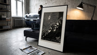 Bound man swarmed by rats print in a slim black frame leaning on a dark sofa in a concrete print studio