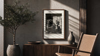 seated man examined by standing figure poster framed above a fluted sideboard beside an olive tree