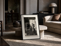 seated man examined by standing figure print in a black frame leaning on a travertine table in a sunlit lounge