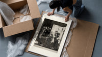seated man examined by standing figure framed print being unpacked from protective bubble wrap and a box