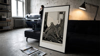 Snarling ape attacking woman print in a slim black frame leaning on a dark sofa in a concrete print studio