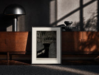 Black-framed Man dragging woman toward water print on a moody console with designer coffee-table books
