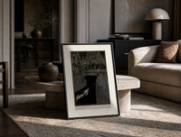 Man dragging woman toward water print in a black frame leaning on a travertine table in a sunlit lounge