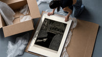 Man dragging woman toward water framed print being unpacked from protective bubble wrap and a box