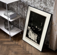 Decaying corpse on bed with figures poster in a black frame leaning beside a shelf in a raw-plaster loft