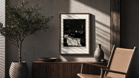 Decaying corpse on bed with figures poster framed above a fluted sideboard beside an olive tree