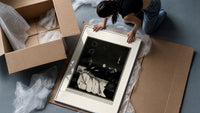 Decaying corpse on bed with figures framed print being unpacked from protective bubble wrap and a box