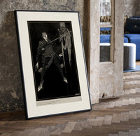 Two men in a sword duel print in a black frame leaning beside a vintage door on parquet