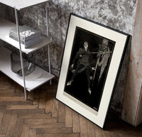 Two men in a sword duel poster in a black frame leaning beside a shelf in a raw-plaster loft