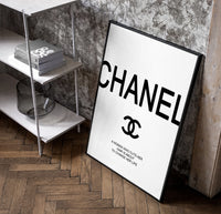 Chanel logo with quote poster in a black frame leaning beside a shelf in a raw-plaster loft