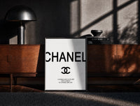 Black-framed Chanel logo with quote print on a moody console with designer coffee-table books