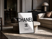 Chanel logo with quote print in a black frame leaning on a travertine table in a sunlit lounge