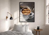 Coffee and an Open Book print in a black frame above a bed with striped linens, a brass wall lamp and a sunlit window