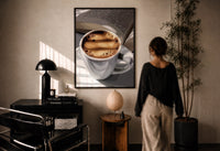 Coffee and an Open Book print in a black frame on a sunlit plaster wall, a woman looking on beside a mushroom lamp