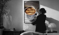 Coffee and an Open Book print in a slim black frame being hung on a sunlit wall in a monochrome room