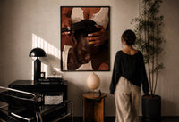 Combing Hair with Painted Nails print in a black frame on a sunlit plaster wall, a woman looking on beside a mushroom lamp
