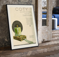 Green perfume bottle on box print in a black frame leaning beside a vintage door on parquet