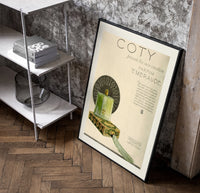 Green perfume bottle on box poster in a black frame leaning beside a shelf in a raw-plaster loft