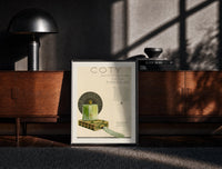 Black-framed Green perfume bottle on box print on a moody console with designer coffee-table books