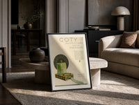 Green perfume bottle on box print in a black frame leaning on a travertine table in a sunlit lounge