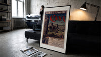 Medieval castle ruins with tower print in a slim black frame leaning on a dark sofa in a concrete print studio