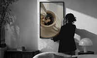 Cream Poured into Black Coffee print in a slim black frame being hung on a sunlit wall in a monochrome room