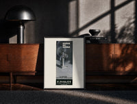 Black-framed Perfume bottle on pedestal print on a moody console with designer coffee-table books