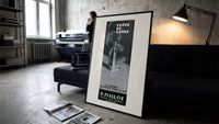 Perfume bottle on pedestal print in a slim black frame leaning on a dark sofa in a concrete print studio