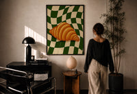 Croissant on Green Checkerboard print in a black frame on a sunlit plaster wall, a woman looking on beside a mushroom lamp