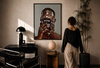 Dangling Jewelry Over the Face print in a black frame on a sunlit plaster wall, a woman looking on beside a mushroom lamp