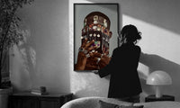 Dangling Jewelry Over the Face print in a slim black frame being hung on a sunlit wall in a monochrome room