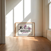 Woman smelling lilac flowers print in an oak frame on a sunlit wood floor beneath tall window light