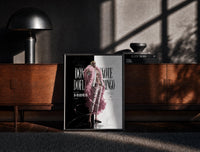 Black-framed blond man in pink feather coat print on a moody console with designer coffee-table books