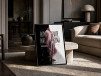 blond man in pink feather coat print in a black frame leaning on a travertine table in a sunlit lounge