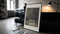 Gathering of robed classical poets print in a slim black frame leaning on a dark sofa in a concrete print studio