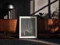 Black-framed Two robed figures on cliff ledge print on a moody console with designer coffee-table books