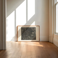Winged demon Lucifer in underworld cavern print in an oak frame on a sunlit wood floor beneath tall window light