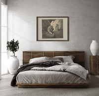 Crouching giant and two robed figures print in a dark wood frame above a rattan bed on a plaster wall