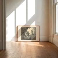 Crouching giant and two robed figures print in an oak frame on a sunlit wood floor beneath tall window light