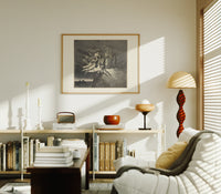 winged demons and two robed figures print in an oak frame above a mid-century book console with a vintage radio