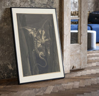Winged monster carrying two figures print in a black frame leaning beside a vintage door on parquet
