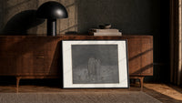 Two robed figures among buried heads print in a black frame leaning against a walnut console in lamplight