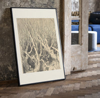 Faces in gnarled bare trees print in a black frame leaning beside a vintage door on parquet