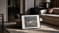 Two robed figures among hooded crowd print in a slim black frame leaning on a travertine coffee table