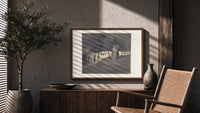 Two robed figures among hooded crowd print in a wood frame above a fluted sideboard beside an olive tree