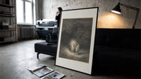 Glowing woman and robed figure print in a slim black frame leaning on a dark sofa in a concrete print studio