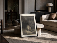 Glowing woman and robed figure print in a black frame leaning on a travertine table in a sunlit lounge